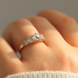 May include: A gold band ring with a row of sparkling diamonds. The ring features a larger, central diamond surrounded by smaller diamonds.