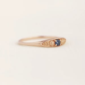 Pu&ograve; includere: Un delicato anello in oro rosa con una pietra preziosa blu circondata da dettagli floreali.