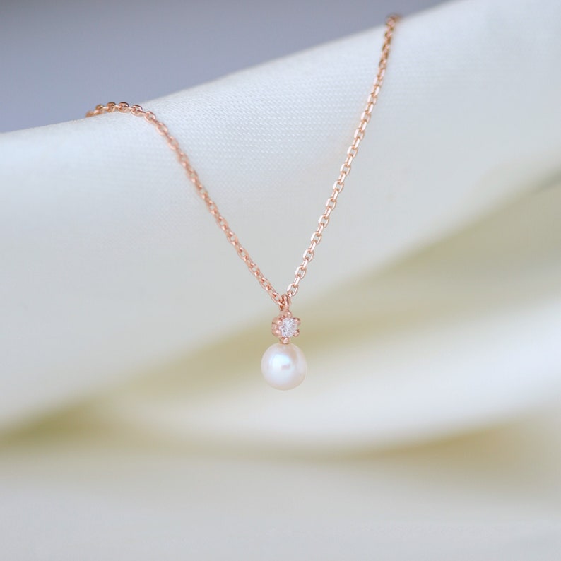 May include: A delicate rose gold necklace with a single pearl pendant and a small diamond accent.