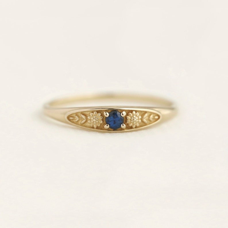 Pu&ograve; includere: Un anello d'oro con una pietra preziosa blu e dettagli floreali.