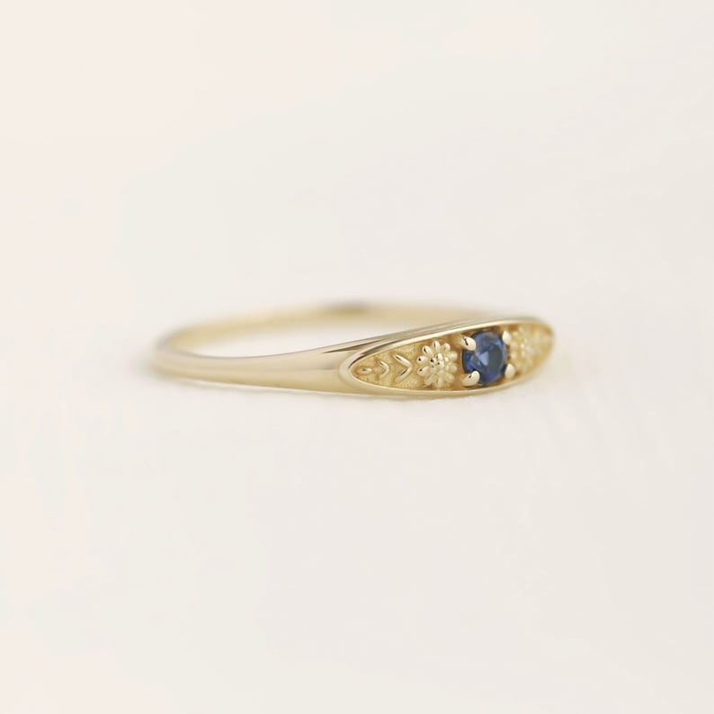 Pu&ograve; includere: Un anello d'oro con una pietra preziosa blu e dettagli floreali.