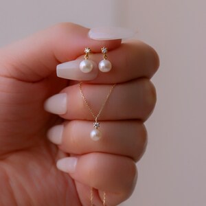 May include: A delicate gold necklace and earrings set featuring a small pearl and a tiny diamond accent. The necklace has a simple chain and the earrings are drop style.