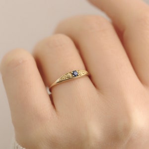 Pu&ograve; includere: Un delicato anello d'oro con una piccola pietra preziosa blu incastonata al centro. La fascia &egrave; decorata con un motivo floreale.