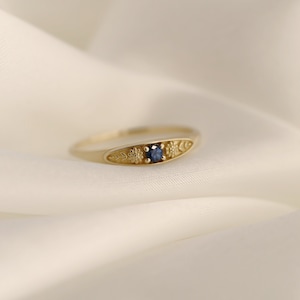 Pu&ograve; includere: Un anello d'oro con un delicato design floreale e un piccolo zaffiro blu.