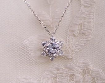 May include: A silver necklace featuring a snowflake pendant. The pendant is adorned with multiple clear, sparkling crystals, creating a brilliant, eye-catching design. The necklace hangs on a delicate silver chain, perfect for adding a touch of elegance.