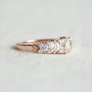 May include: A rose gold engagement ring with a cluster of round diamonds. The center stone is a large, cushion-cut diamond.