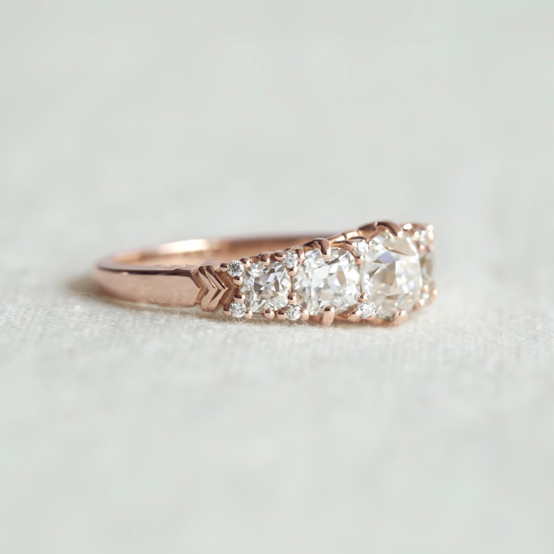 May include: A rose gold engagement ring with a cluster of round diamonds. The center stone is a large, cushion-cut diamond.
