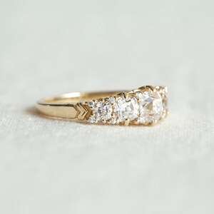 May include: A gold band ring with a row of three large, round, bezel-set diamonds and smaller diamonds set in the band.