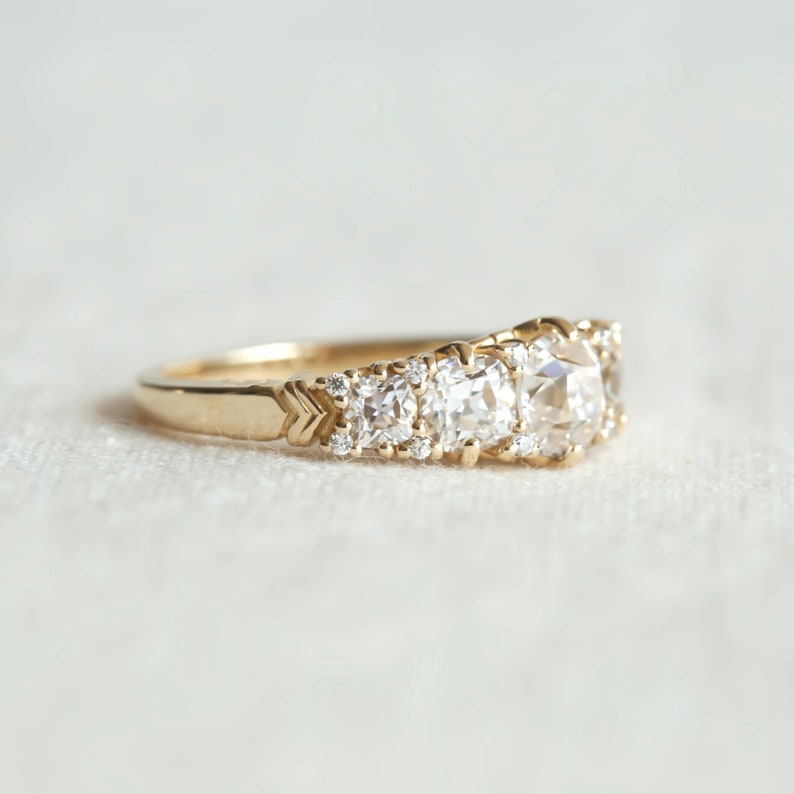 May include: A gold band ring with a row of three large, round, bezel-set diamonds and smaller diamonds set in the band.