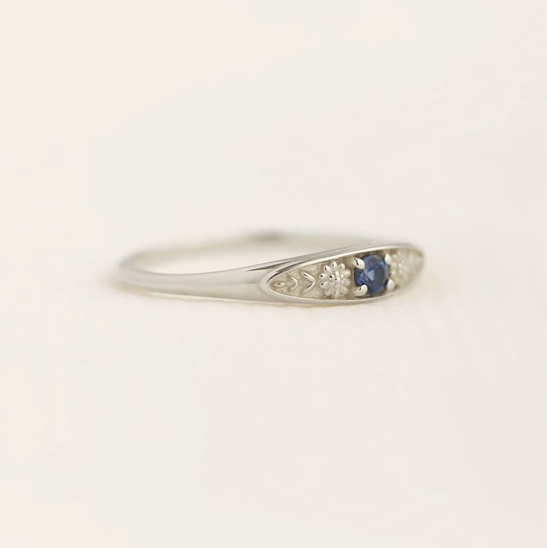 Pu&ograve; includere: Un anello d'argento con una pietra preziosa zaffiro blu e dettagli floreali.