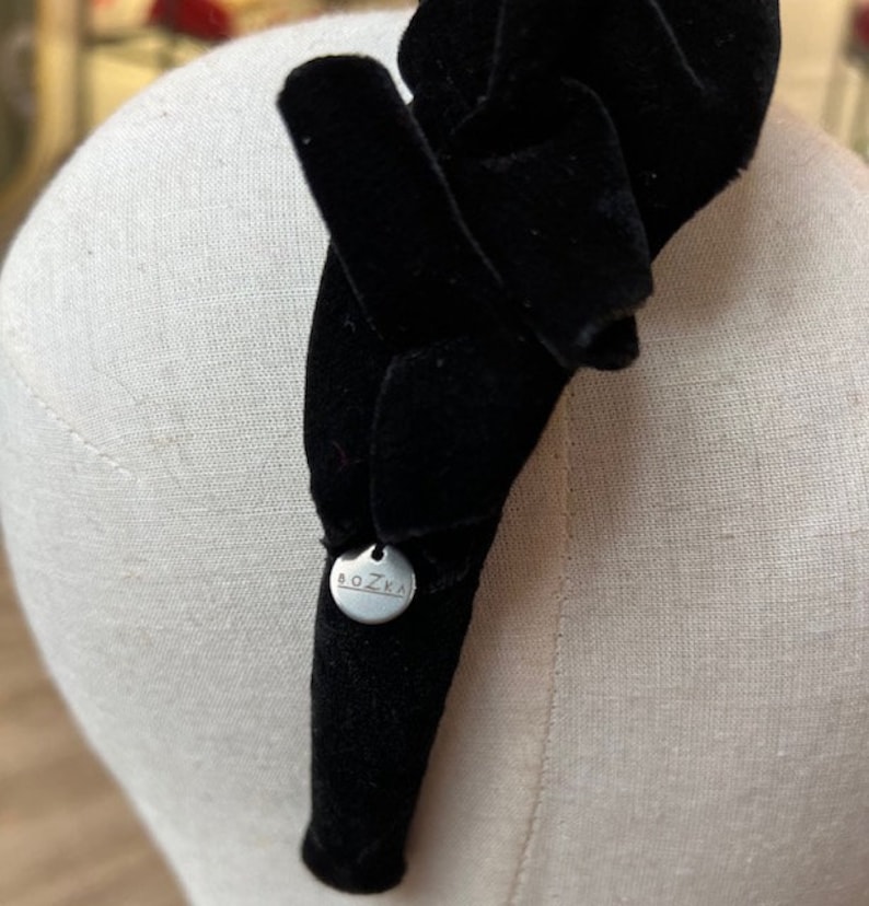Puede incluir: Diadema de terciopelo negro con una etiqueta de metal plateado que dice "BOZKA".