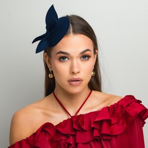 Peut inclure: Une femme portant un haut rouge à volants avec un accessoire pour cheveux en forme de fleur en feutre bleu marine.