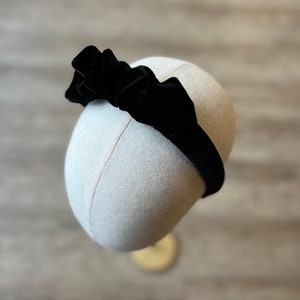 Puede incluir: Una diadema de terciopelo negro con un gran lazo fruncido. La diadema est&aacute; en una cabeza de maniqu&iacute;.