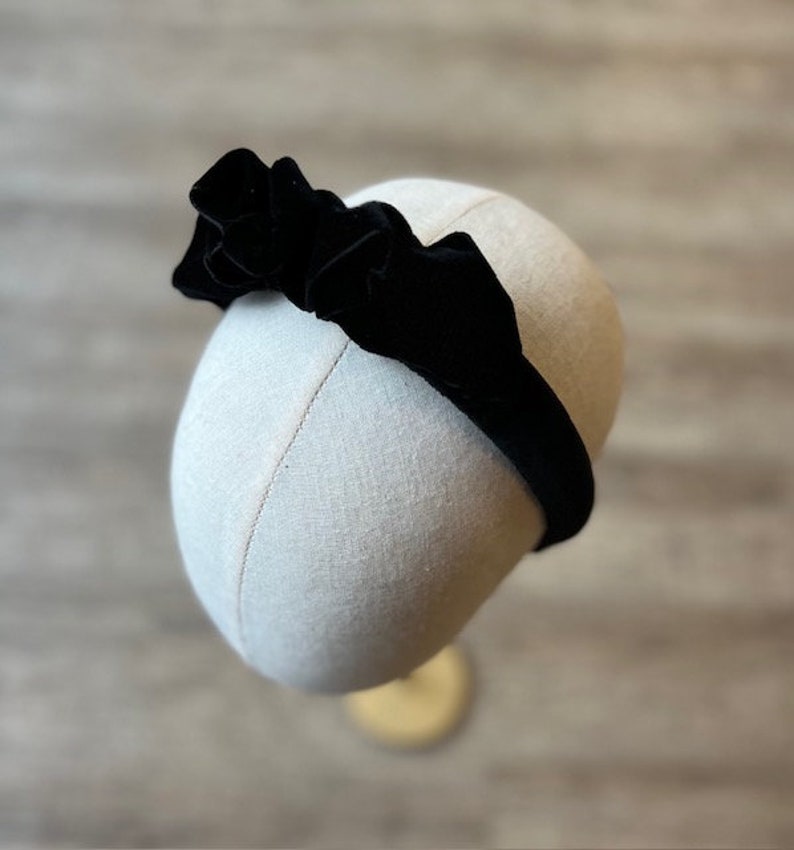 Puede incluir: Una diadema de terciopelo negro con un gran lazo fruncido. La diadema est&aacute; en una cabeza de maniqu&iacute;.