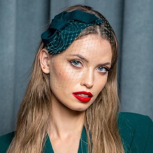 May include: A woman wearing a green velvet hat with a veil and a green blazer.