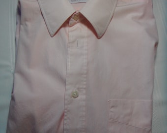 May include: A pale pink long-sleeved button-down shirt with a white collar and a pocket on the left side. The shirt has the text "Bonwit Teller Men's Shop" on the label.