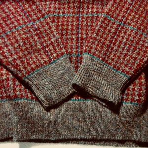May include: A red, blue and grey patterned sweater with a ribbed knit cuff and hem.