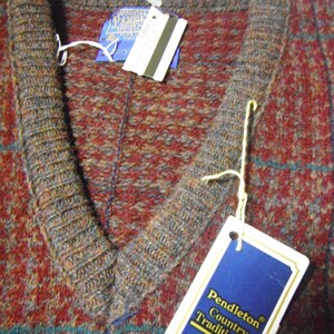 May include: A Pendleton Country Traditionals V-neck sweater in a red, brown and blue plaid pattern. The tag reads "Pendleton Country Traditionals 100% Virgin Wool".
