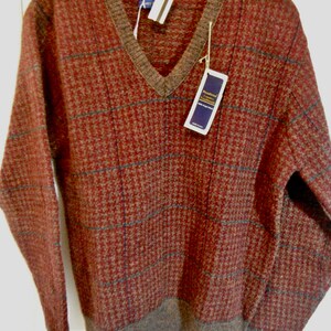 May include: A brown and tan plaid V-neck sweater with a brown ribbed collar and cuffs. The sweater has a tag that reads "Traditional Luxury Textiles 100% Pure New Wool".