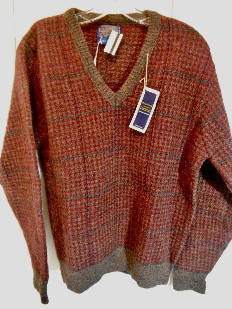May include: A brown and tan plaid V-neck sweater with a brown ribbed collar and cuffs. The sweater has a tag that reads "Traditional Luxury Textiles 100% Pure New Wool".