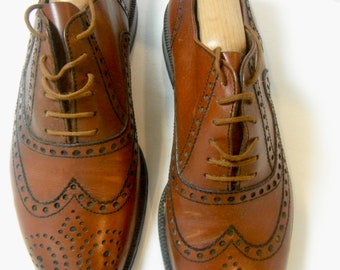 May include: A pair of brown leather brogue shoes with a lace-up fastening. The shoes feature a wingtip design and a perforated pattern.