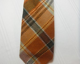 May include: A brown, beige, and gray plaid tie. The tie has a pointed tip and is made of a woven fabric.