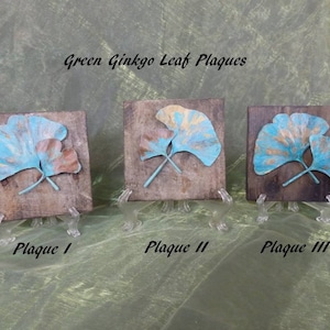 May include: Three wooden plaques with a raised design of two green and gold ginkgo leaves. The plaques are labeled "Plaque I", "Plaque II", and "Plaque III".