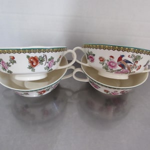 May include: Set of four vintage soup bowls with floral and bird designs. The bowls are white with green, gold, and pink accents. The bowls are stacked in two pairs.