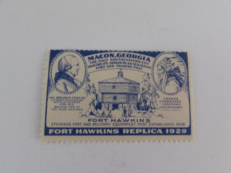 May include: A blue and white vintage postcard depicting Fort Hawkins, a stockade fort and military equipment post established in 1806 in Macon, Georgia. The postcard features a drawing of the fort, a portrait of Col. Benjamin Hawkins, and a portrait of a Native American. The text on the postcard reads "Fort Hawkins Replica 1929".