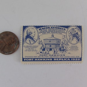 May include: A vintage postcard replica of Fort Hawkins in Macon, Georgia. The postcard features a blue and white illustration of the fort, a portrait of Colonel Benjamin Hawkins, and a portrait of a Native American chief. The text on the postcard reads "Macon, Georgia, The Only Southeastern City Tracing Its Origin to an Old Indian Fort and Trading Post."  "Fort Hawkins, Stockade Fort and Military Equipment Post - Established 1806."  "Fort Hawkins Replica 1929."