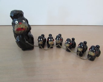May include: A black ceramic poodle figurine with a chain attached to seven smaller black ceramic poodle figurines. The figurines are all facing the same direction and the chain is connected to each of their necks.