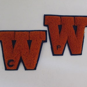 May include: Two felt letter patches in the shape of the letter W. The patches are orange with a navy blue outline. The letter on the left has a C in the bottom left corner. The letter on the right has a P in the bottom left corner.