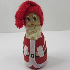 May include: A wooden Santa Claus figurine with a red knitted hat, white beard, and red and white painted clothing.
