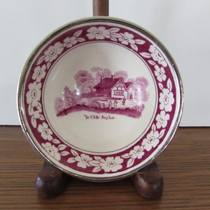 May include: A white ceramic bowl with a pink floral border and a pink illustration of a house with the text "Ye Olde Jug Inn".