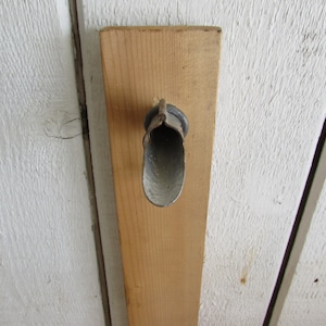 May include: A close-up of a metal, gray,  pipe-like object attached to a wooden board. The object is shaped like a funnel with a rounded opening.
