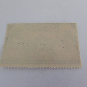 May include: A blank, off-white postage stamp with a scalloped edge. The stamp has a faint blue tint and some light brown spots.