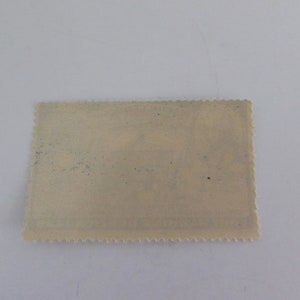 May include: A vintage postage stamp with a faded design and a scalloped edge.