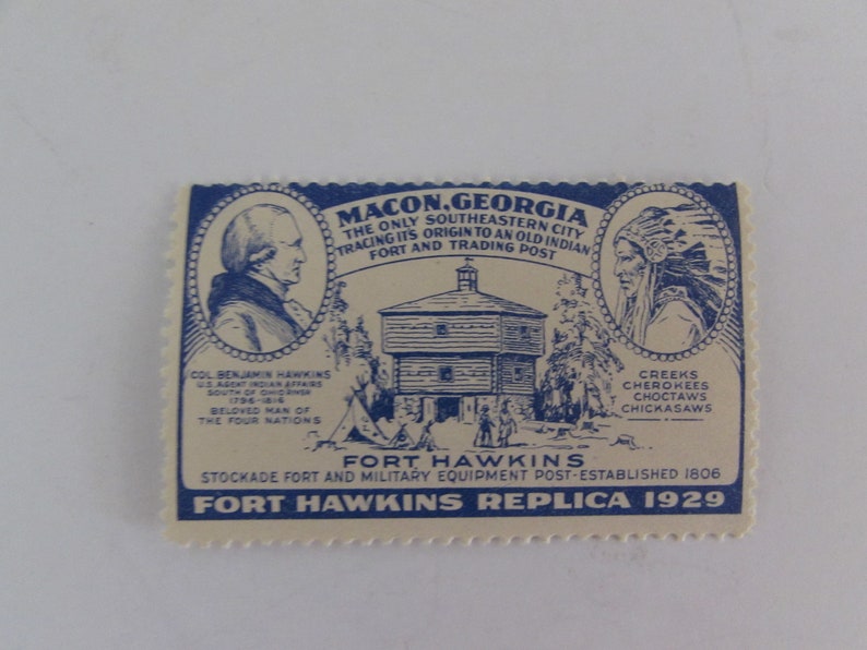May include: A blue and white vintage stamp commemorating Fort Hawkins in Macon, Georgia. The stamp features a drawing of the fort, a portrait of Col. Benjamin Hawkins, and a portrait of a Native American. The text on the stamp reads "Macon, Georgia, The Only Southeastern City Tracing Its Origin to an Old Indian Fort and Trading Post", "Fort Hawkins", "Stockade Fort and Military Equipment Post-Established 1806", and "Fort Hawkins Replica 1929".