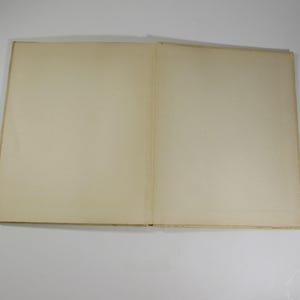 May include: A blank, off-white book with a cream-colored spine. The book is closed and lying flat on a white surface.