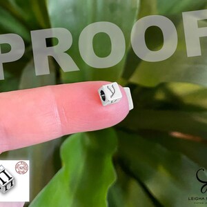 May include: A small silver cube-shaped bead featuring a black engraved Greek letter pi on its side. The bead has a central hole for threading. An inset diagram shows the bead measures 5.5 mm by 4.0 mm and includes a 925 sterling silver stamp.