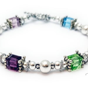 May include: A silver bracelet with a variety of colored square beads and silver round beads. The bracelet has a clasp closure.