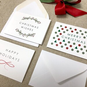 May include: Three Christmas cards with white backgrounds and different designs. The first card has a green wreath with red berries and the text "Christmas Wishes". The second card has a red ribbon and the text "Merry Christmas". The third card has a red infinity symbol and the text "Happy Holidays".