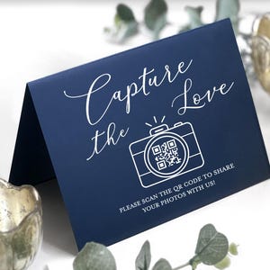 May include: A navy blue card with the text "Capture the Love" in elegant script. A white camera graphic with a QR code is below the text. The card reads "Please scan the QR code to share your photos with us!"