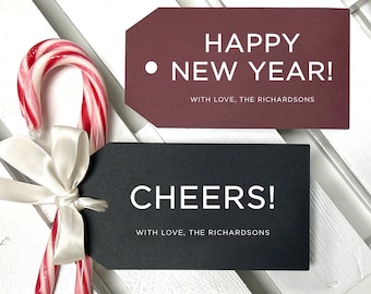 May include: Two rectangular gift tags with white text. One is burgundy with "HAPPY NEW YEAR! WITH LOVE, THE RICHARDSONS" and the other is black with "CHEERS! WITH LOVE, THE RICHARDSONS". A red and white candy cane with a white ribbon is attached.
