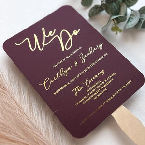 May include: Burgundy wedding fan with gold lettering. The fan reads "We Do" and includes the names "Caitlyn & Zachary" and the wedding date "November 16, 2024". The fan also includes the ceremony details: "The Ceremony", "Processional", "Exchange of Vows", "Exchange of Rings", "Pronouncement of Marriage", "Recessional". The fan also includes the reception details: "Reception at 7:00pm at "Diamond Club Poolside."