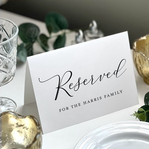 May include: White card with black calligraphy that reads "Reserved for the Harris Family".