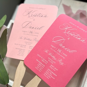 May include: Two wedding fans, one light pink and one hot pink, with wooden handles. Each fan features elegant script with the names "Kristina & Daniel" and the date "August 16, 2026". The fans also list the wedding party.