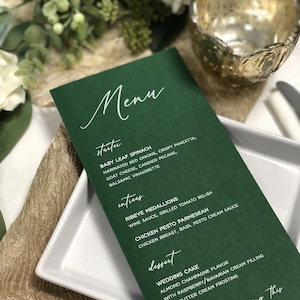 May include: A green menu card with white text listing the menu items for a wedding reception. The menu includes starter, entrees, and dessert options. The text at the bottom reads "Thank you for sharing this special day with us XOXO - Carly and Christopher".