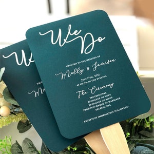 May include: Teal wedding ceremony program fan with white text. The text reads "We Do" and "Welcome to the wedding of Molly & Jamison" followed by the date and time of the ceremony. The program lists the order of events for the ceremony, including the processional, exchange of vows, exchange of rings, pronouncement of marriage, and recessional. The program also includes the information that the reception will immediately follow the ceremony.