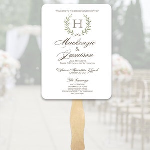 May include: White wedding ceremony program fan with a green wreath and the letter H in the center. The text reads "Welcome to the wedding ceremony of Mackenzie & Jamison June 16th 2019 Three o'clock in the afternoon Spruce Mountain Ranch Larkspur, CO The Ceremony Processional Exchange of vows Exchange of rings Pronouncement of marriage Recessional"